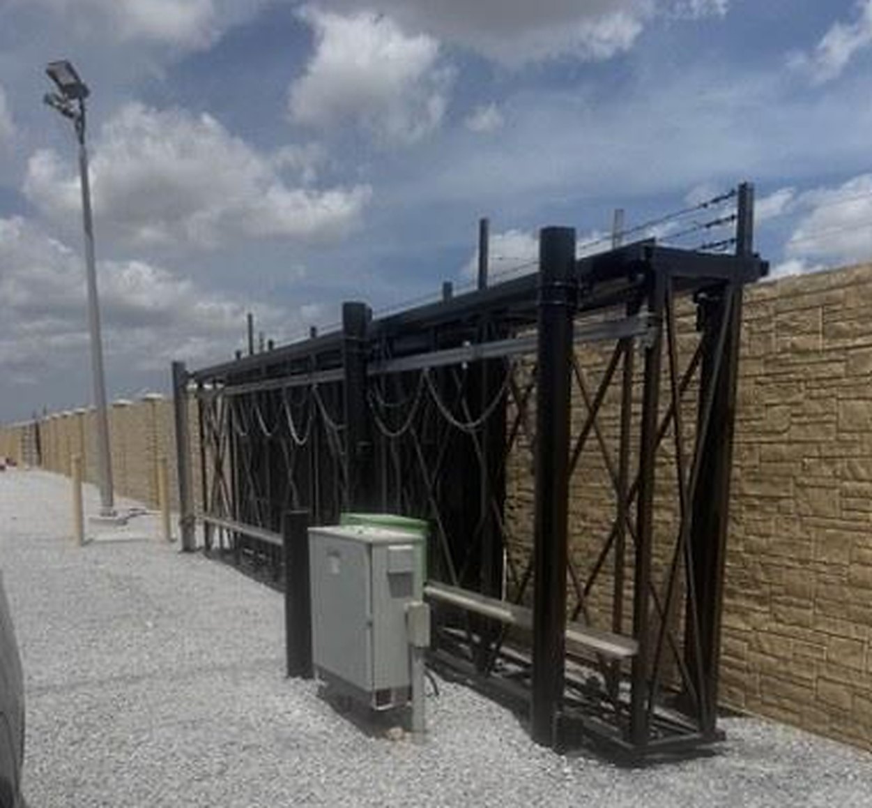 Trait box-framed cantilever gate at a Texas substation: black steel truss leaf on a dual-post carrier with a gate operator, welded wire infill and precast wall behind
